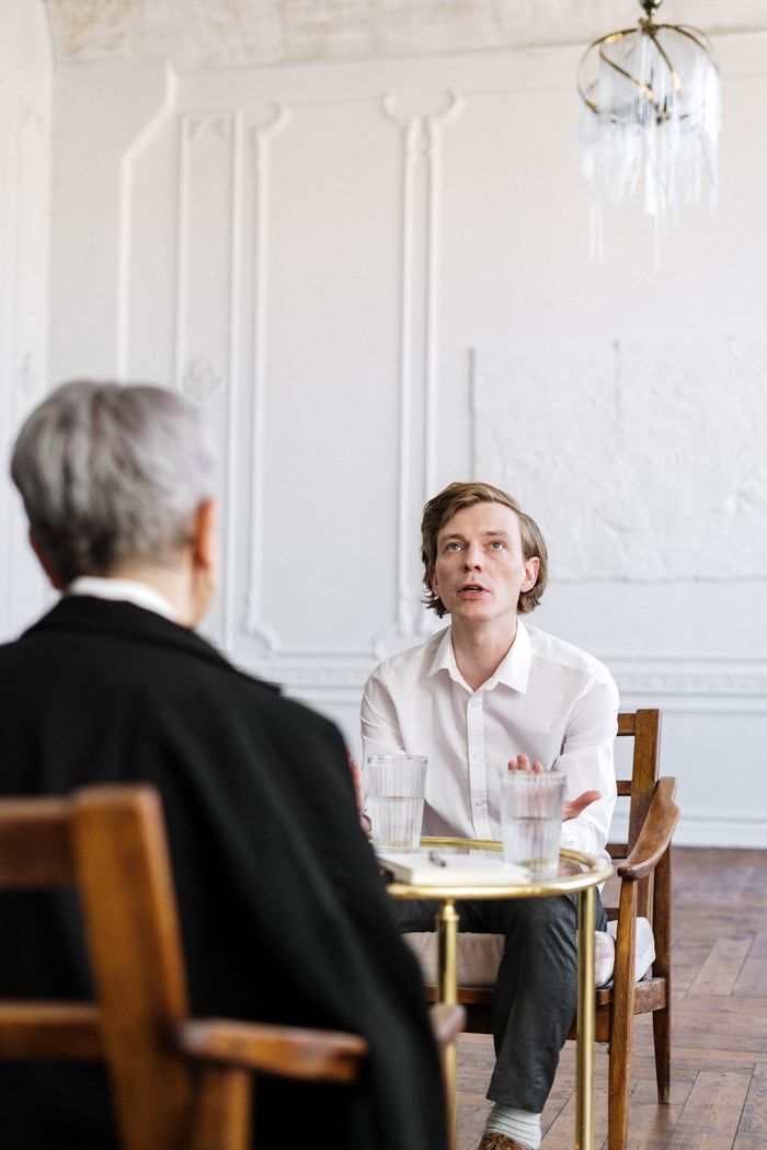Two people in a bright loft, engaged in a counseling session around a glass table.